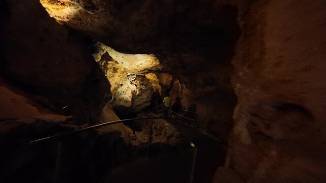 People walking through a dark cave with artificial lighting.