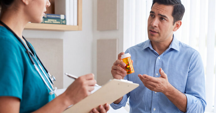 Concerned male patient holding medication bottle while discussing prescription side effects with female doctor in bright clinic office
