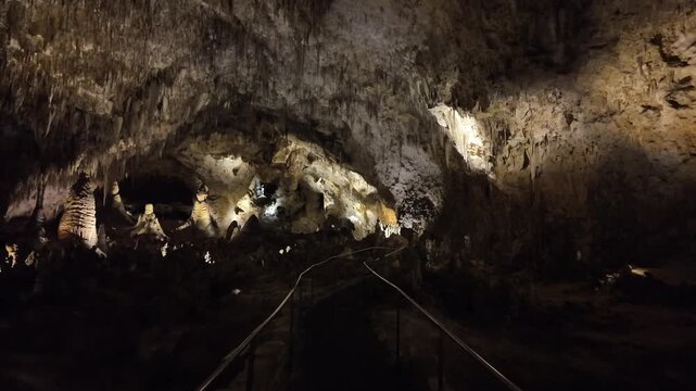 Illuminated cave interior with stalactites and walkway.