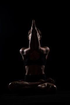 Backlight yoga practitioner holding a forearm stand against a black ba