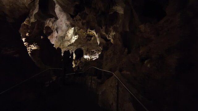 Interior of a lit limestone cave with stalactites and walkway.
