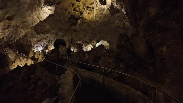 Interior of a lit limestone cave with stalactites and walkway.