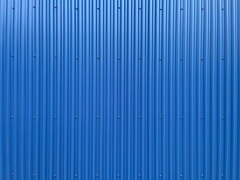 Blue corrugated metal texture background with vertical lines. Corrugated iron siding wall backdrop in vibrant blue. Industrial blue metal sheeting texture for copy space.