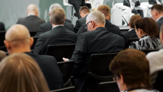Business professionals seated in a conference hall listening to a presentation. Corporate audience attending a seminar, forum or professional business event.