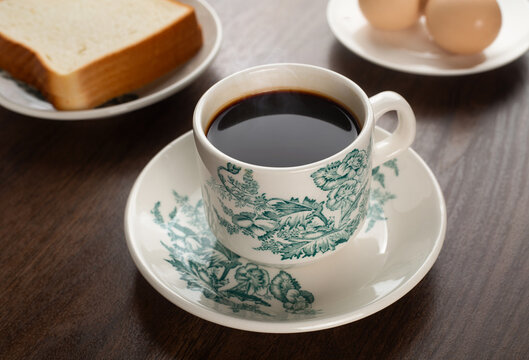 Traditional Malaysian kopitiam black coffee in vintage floral porcelain cup with toast and soft boiled eggs on wooden table