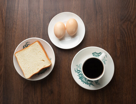 Traditional Malaysian kopitiam breakfast set with toast bread, soft boiled eggs, and black coffee on wooden table top view
