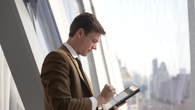Businessman uses digitized pen on digital tablet by office window