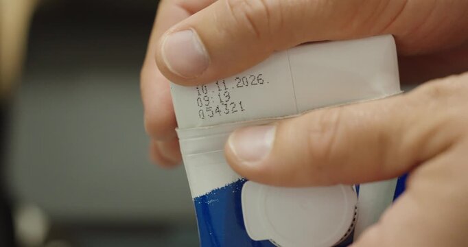 Close-up of a person checking the expiration date and batch number printed on food packaging.