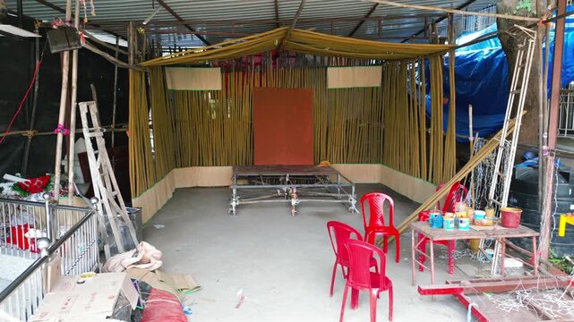 Drone shot view of an empty Ganpati pandal under construction, featuring a wooden platform, red backdrop, and bamboo walls during festival preparation.