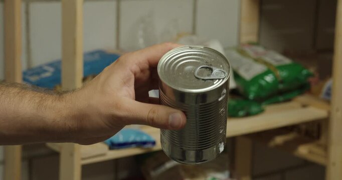Person rotates and inspects an empty metal food can, showing the container from different angles.