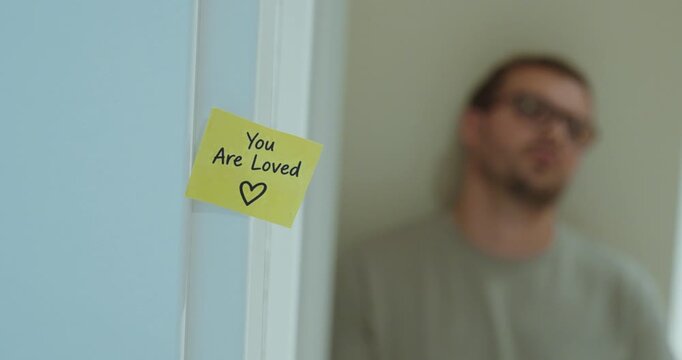 Man standing thoughtfully in the background with a positive &ldquo;You Are Loved&rdquo; message in focus.