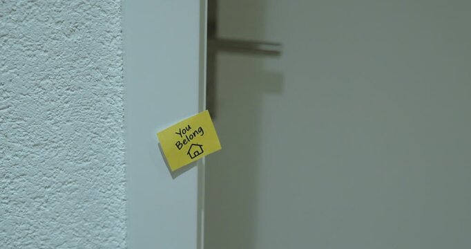 Person sticks a You Belong Here note near a door, representing belonging, welcome and inclusion.