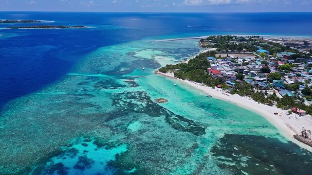 High angle drone perspective of local island town and white beach bordering vibrant coral reef sea. Ideal visual asset for travel guides, destination, and holiday videos.Himmafushi island.Maldives