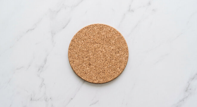 Round brown cork coaster centered on white marble tabletop in top view flat lay for drink protection and table decor