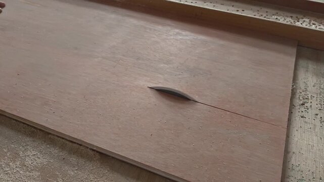 Close up of a circular table saw blade cutting through a sheet of plywood in a woodworking shop with sawdust scattered around the work area.