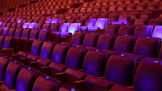 cinematic shot of empty rows of theater seats illuminated by dramatic red and purple stage lighting before a performance or event