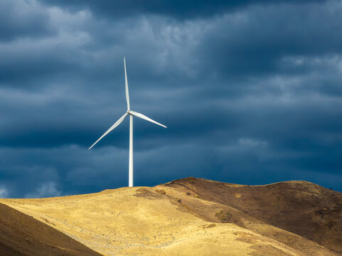 Wind turbine silhouetted against moody sky on arid landscape