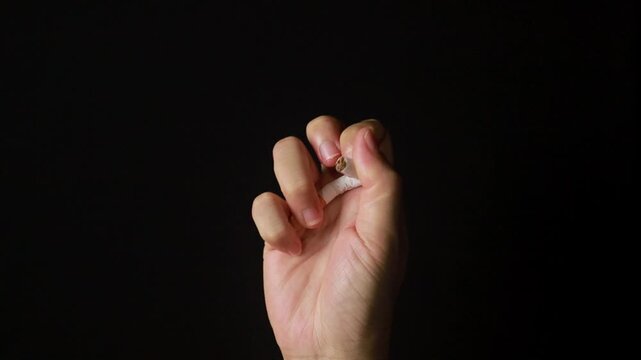 Hand crushing a cigarette to quit smoking on a black background