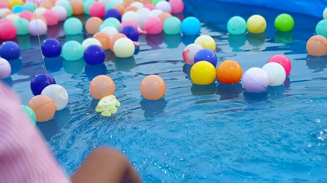 Child's Hand Playing with Colorful Balls and Floating Toy in Blue Water Pool