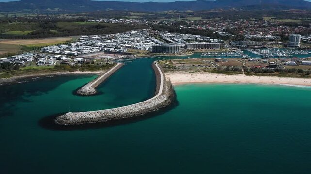 Cross panning view of the idyllic Shell Cove breakwater and turquoise blue entrance leading to the scenic Shellharbour Marina and beach, situated on the Illawarra South Coast of New South Wales.