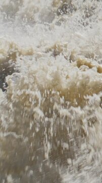 Fierce, muddy water crashes violently in chaotic motion. White froth explodes upward with forceful energy. Turbulent flow suggests rapid current or dam break. Ideal for scenes needing raw