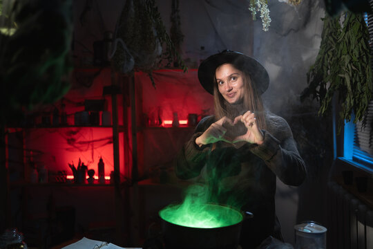 Realistic witch brewing a potion in cauldron showing heart love flirty gesture on camera. Blend of everyday life with traditional witchcraft, magic and mystical atmosphere