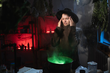 Realistic witch brewing a potion in cauldron looking at camera suffering migraine and headache from stress. Blend of everyday life with traditional witchcraft, magic and mystical © Andrii Lysenko