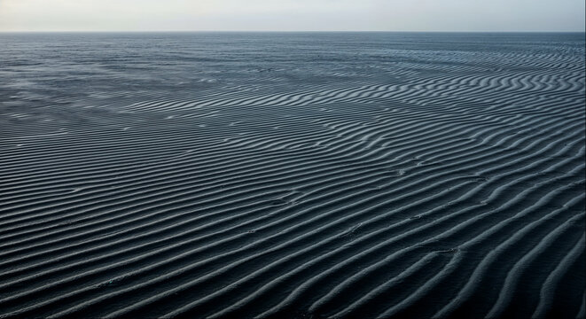 Minimalist dark sand ripples pattern stretching to horizon on black beach