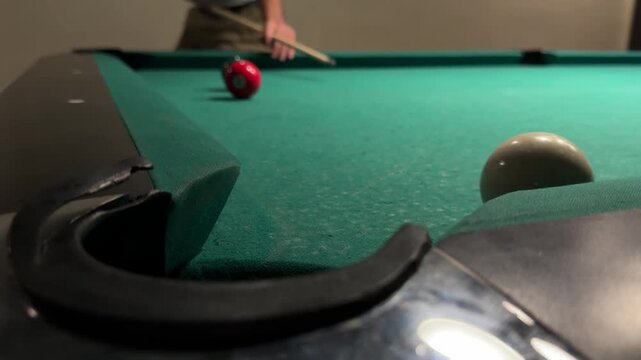 Pool Ball Rolling into a Corner Pocket on a Teal Billiard Table, Close View at Table Level with Other Balls on the Felt and a Player Holding a Cue in the Blurred Background, Horizontal Video
