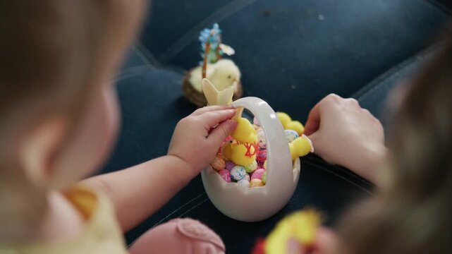 Child plays with colorful plastic ducks and Easter eggs on a sofa. Little hands sort and place yellow ducks into a pink egg-shaped container. Soft focus highlights playful curiosity