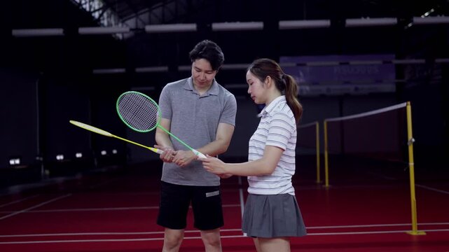 Asian male coach teaching young woman proper badminton racket grip on indoor court