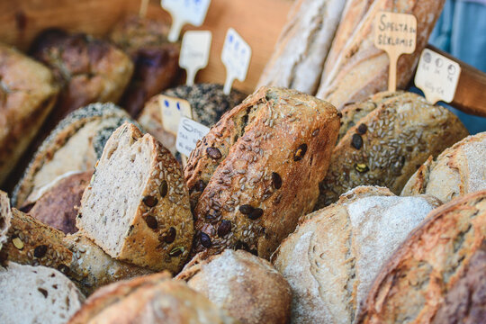 Artisan sourdough bread displayed at a market or bakery, with various types of loaves arranged in a row and featuring small white descriptive cards