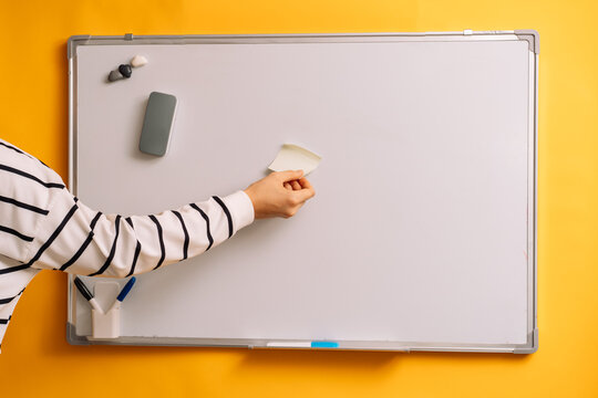 Hand placing a blank sticky note on a whiteboard beside a gray eraser.