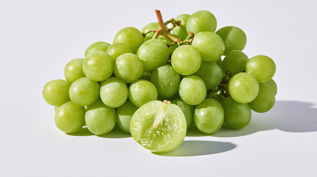 Fresh green grape cluster with plump fruit and sliced grape on pale surface, creating crisp natural food still life with soft shadow