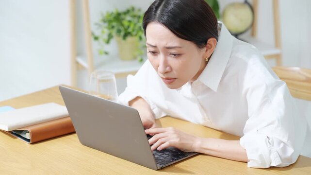 ノートPCにかじりついて見るミドル女性。真剣、仕事、投資、ギャンブル、熱中、集中、仕事、注目、不安