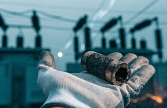 Worker holding a damaged electric component in front of a high voltage power substation
