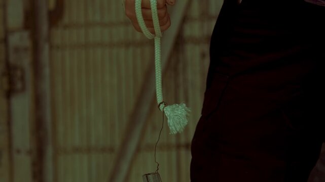 A tense close-up showing a hand tightly gripping a thick rope with a weighted end. The dark, moody lighting highlights themes of street violence, underground crime, and preparation for an urban brawl.