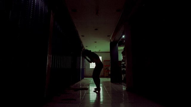 A young woman performs a dramatic, emotional dance in the shadows of a dark, abandoned hallway. The silhouette highlights themes of psychological struggle, artistic expression, and letting go.
