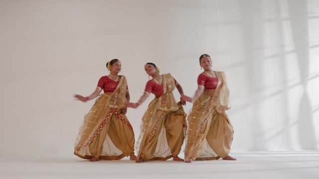 Three Indian women are performing a traditional dance in a studio