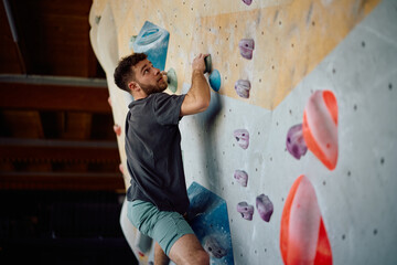 Young athlete practicing indoor climbing on bouldering wall. © Drazen