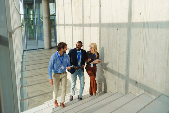 Business team members discussing and smiling while walking up modern office stairs