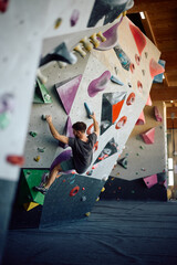 Back view of athlete climbing up the wall during workout in bouldering center.