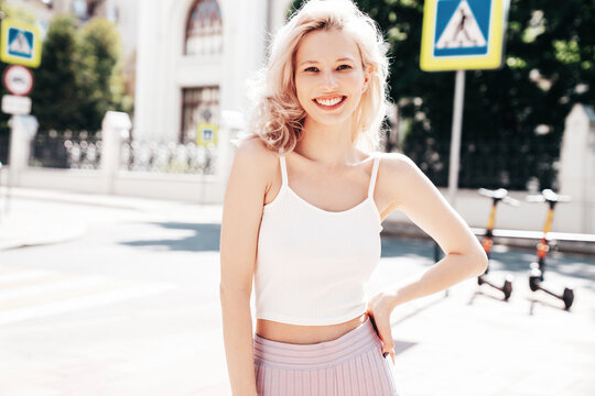 Young beautiful smiling blond hipster woman in trendy summer clothes. Carefree female posing in the street at sunny day. Positive model outdoors at sunset. Cheerful and happy