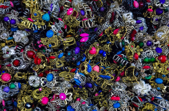 Full frame of colorful vintage-style metal mini hair claws. A pile of small ornate metal hair clips with colorful rhinestones. Top view of a variety of ornate small metal decorative rings with gems
