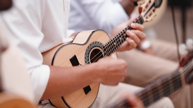 A musician strums a cavaquinho beside a guitarist during a live performance, both dressed in white.