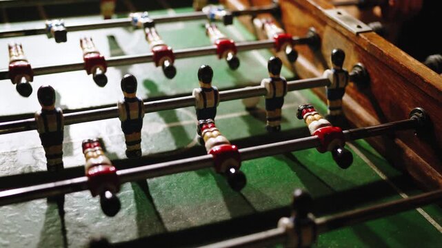 A player grips the rods of an old wooden foosball table, with worn painted figures lined up across the green field.