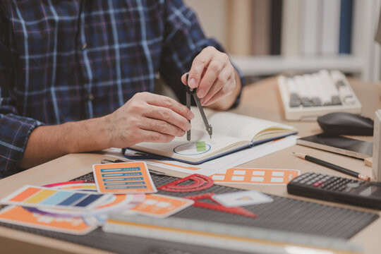 Designer working with color palettes, layout templates, and creative design tools on a desk while planning branding and graphic design projects in a modern office.
