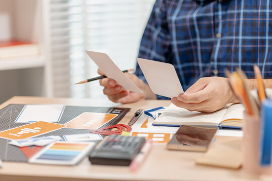 Designer arranging color swatches, layout samples, and branding materials on a creative workspace while planning a visual identity project with notebooks and design tools.