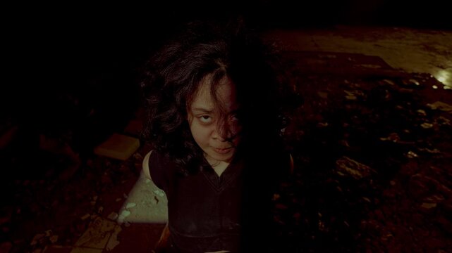 An emotionally drained captive looks down and weeps quietly in the dark after a grueling session of psychological torment. High angle shot depicting utter defeat.