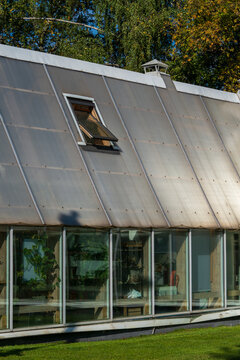 Open roof window in a modern greenhouse. Ventilation hatch on a sloped polycarbonate roof with glass walls and green trees. Garden architecture.